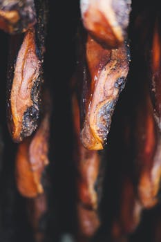 Vertical close-up of smoked meat slices hanging, showing texture and color.