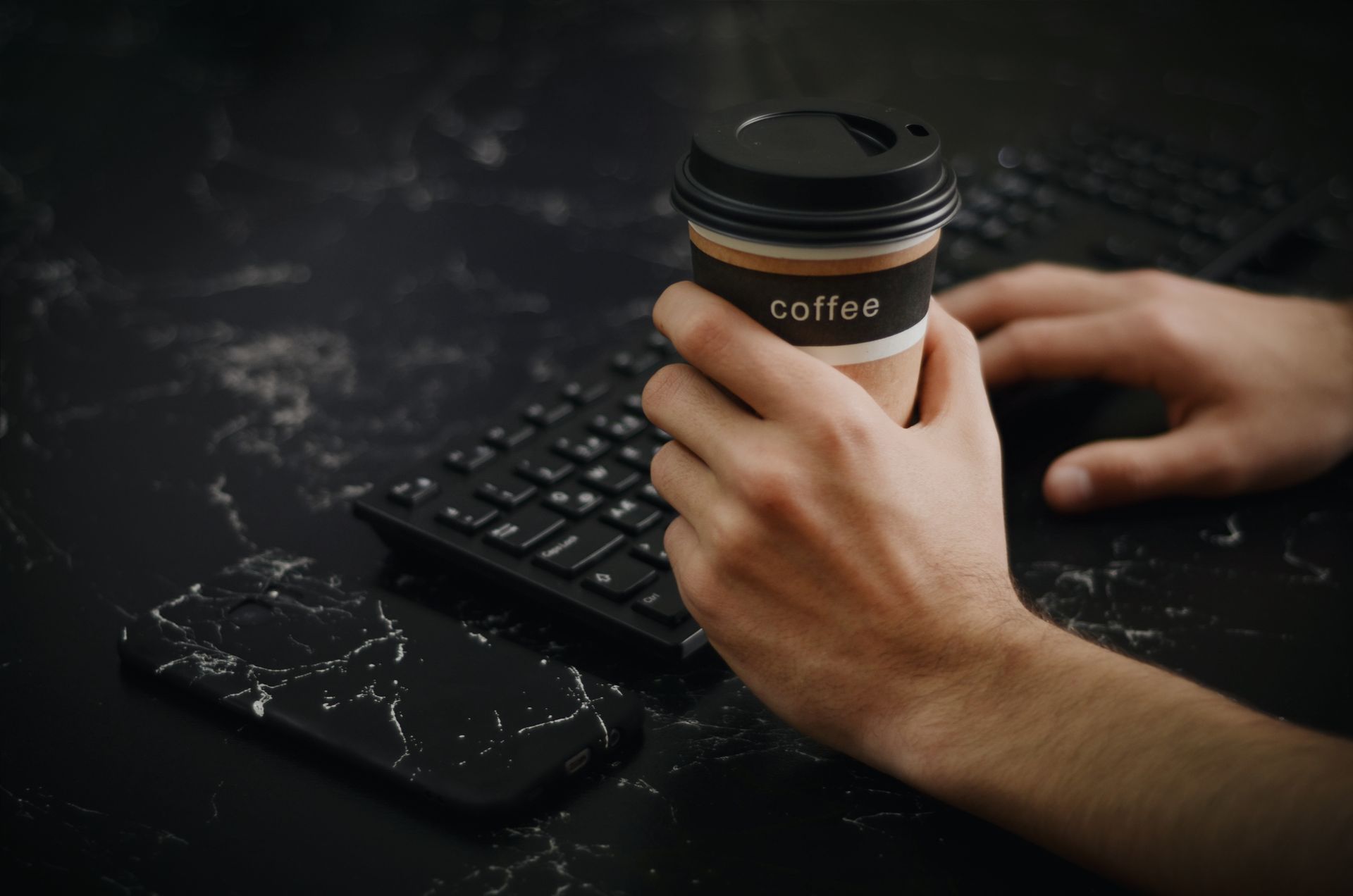Person enjoying a coffee break while typing on keyboard at a stylish workspace.