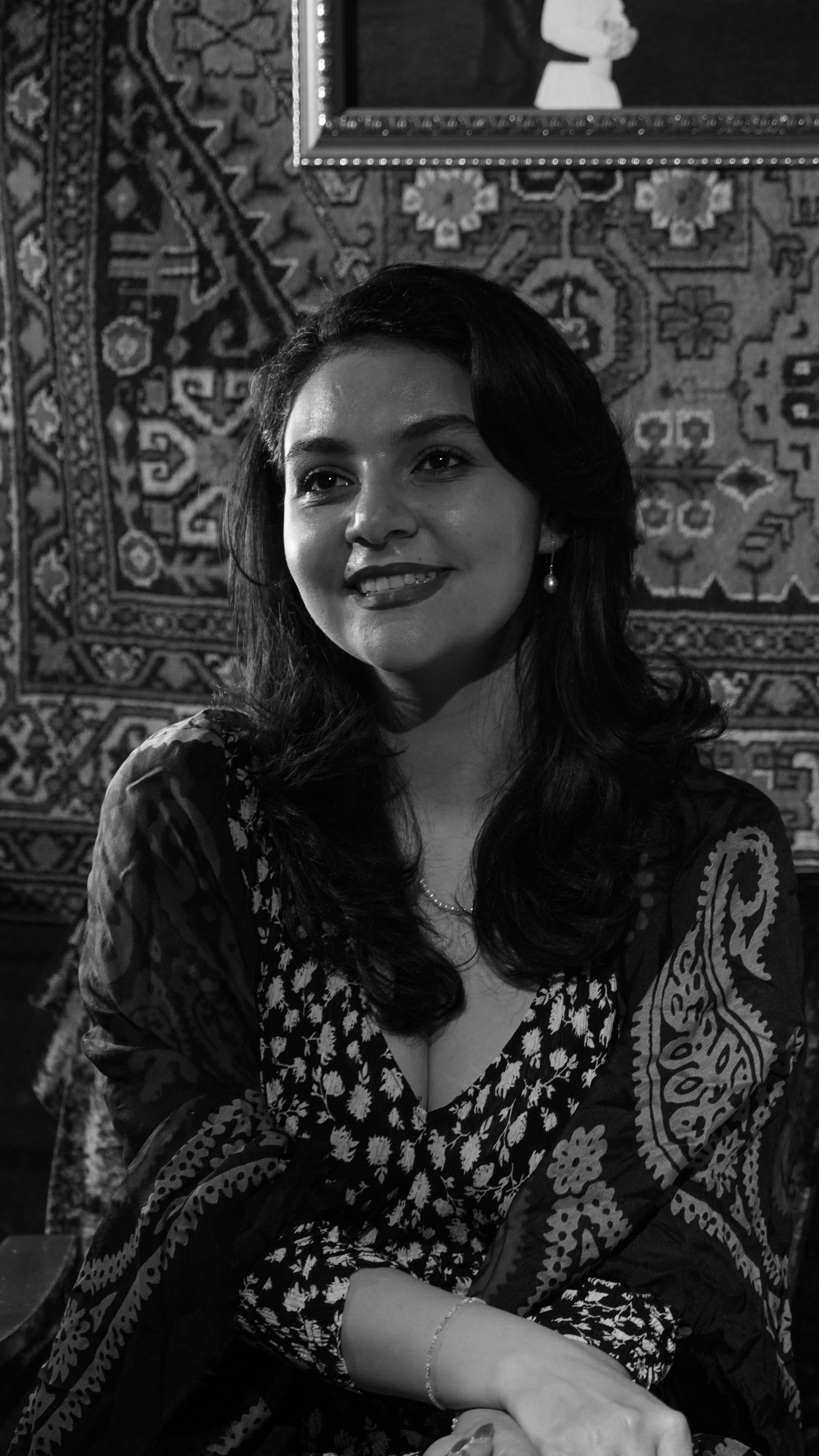 Black and white portrait of a smiling woman in a floral dress, captured indoors in Baku, Azerbaijan.