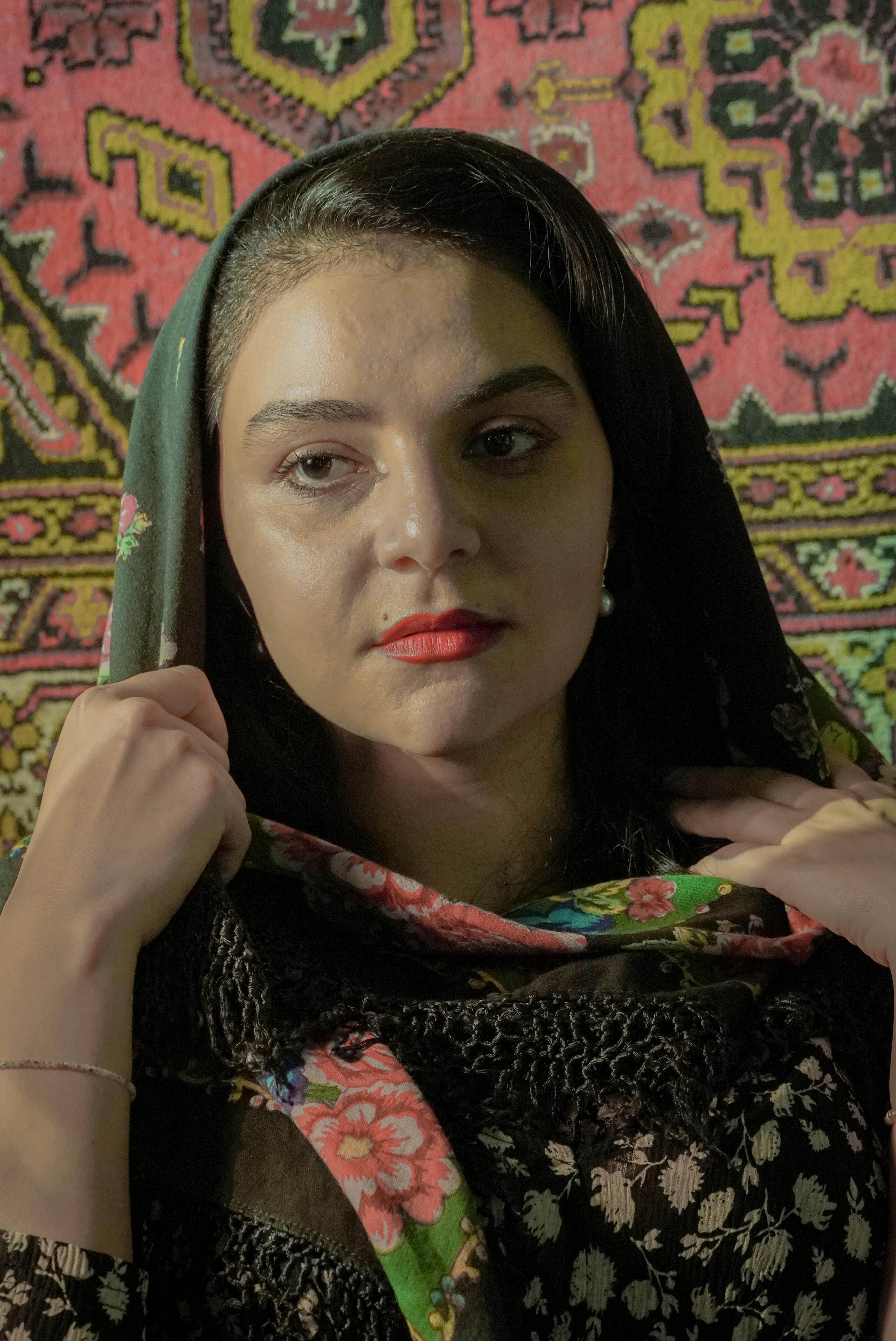 Elegant woman in traditional headscarf posing against a colorful tapestry background.
