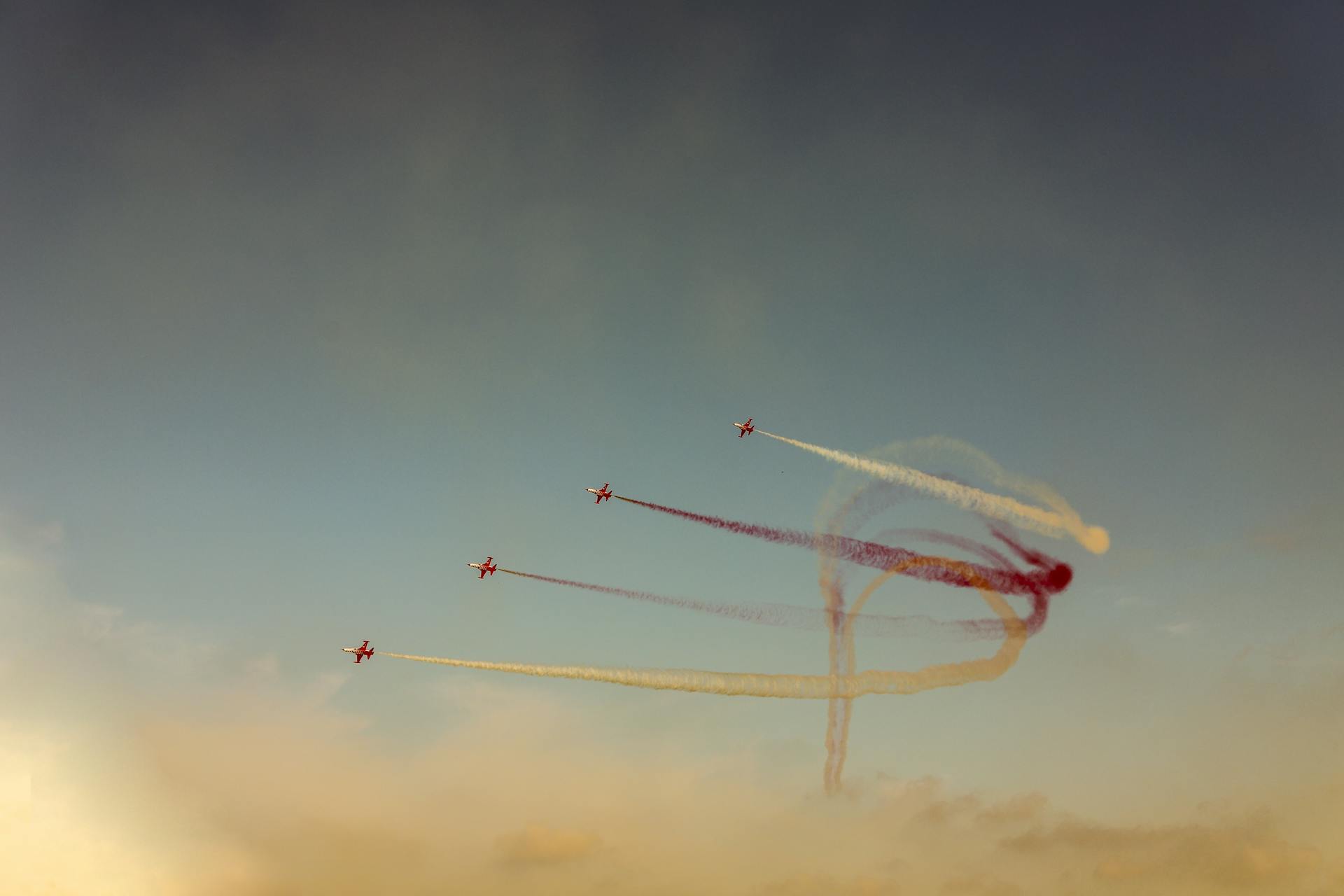 Four fighter jets perform an aerial show with colorful smoke trails against a clear sky.