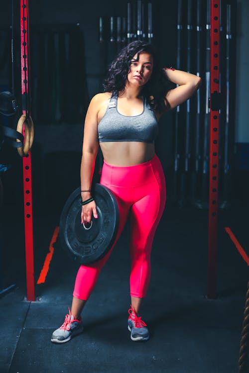 Woman In Grey Sports Bra And Pink Leggings Holding Black Weight Plate