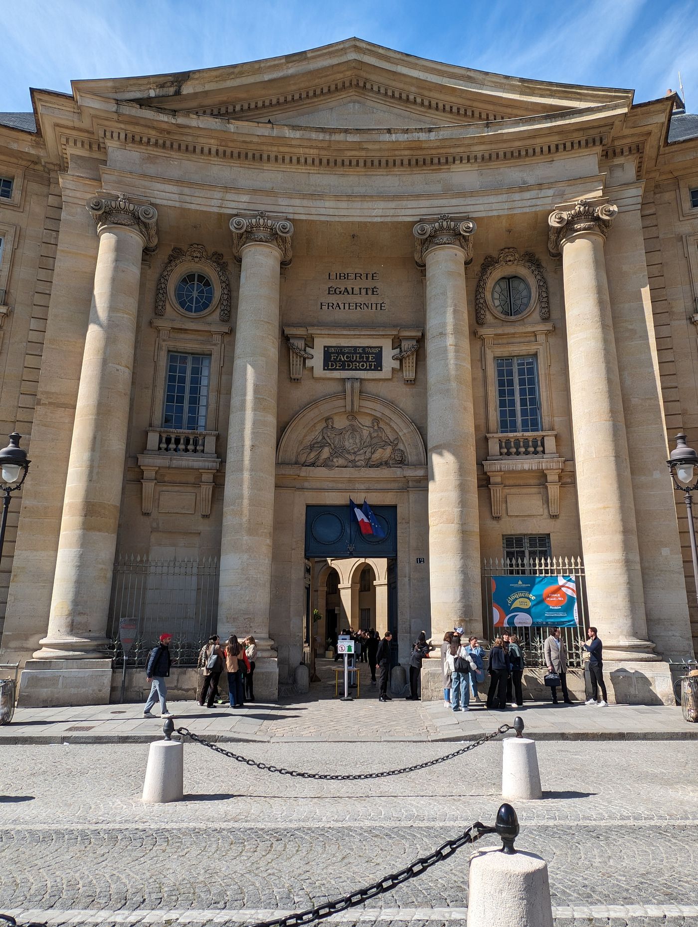 Façade historique d'une faculté parisienne avec des passants devant l'entrée