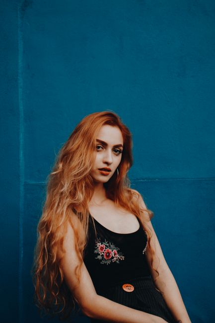 Portrait of a woman with long hair posing elegantly against a bold blue backdrop.