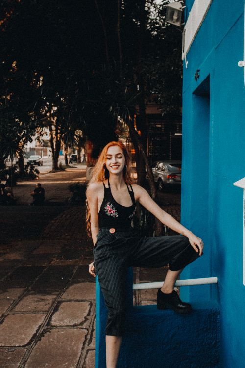 Free Fashionable woman with long hair posing by a vivid blue wall in an outdoor setting. Stock Photo