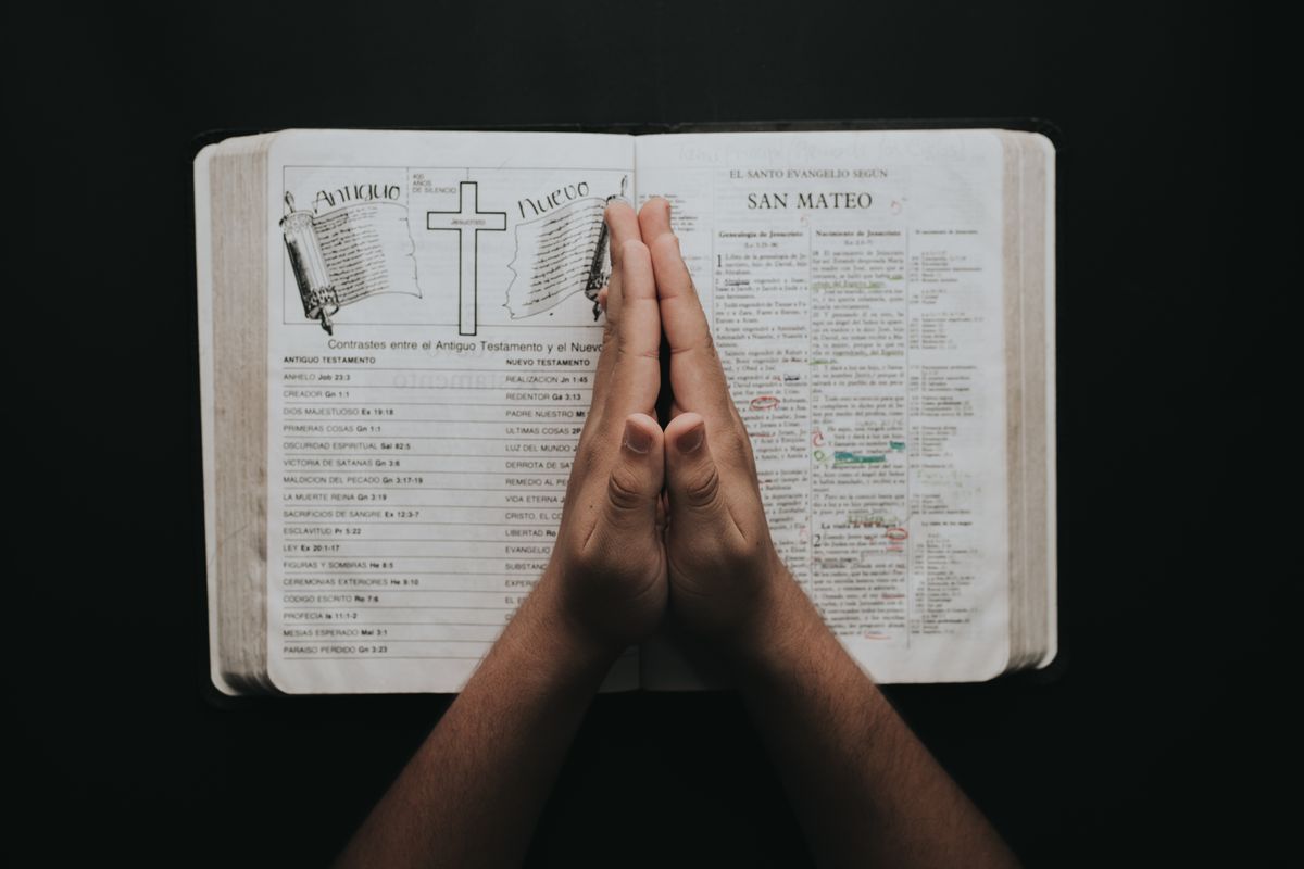 Hands clasped in prayer resting on an open Bible