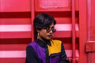 一位时尚女性戴着太阳镜，在现代风格的红色墙壁前摆出姿势，展现着她的风格与态度