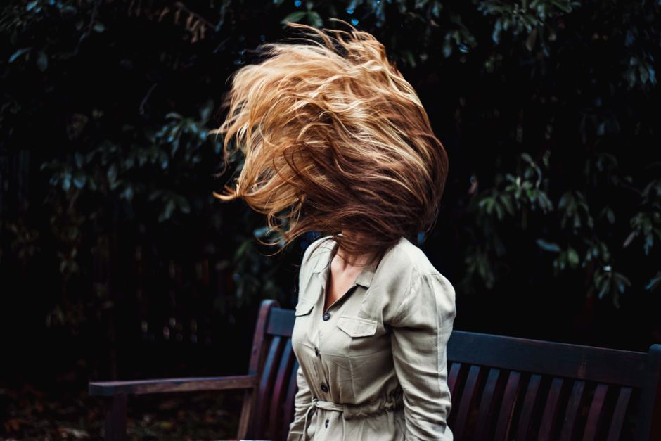 A dynamic photo of a woman flipping her hair while sitting on a park bench outdoors.