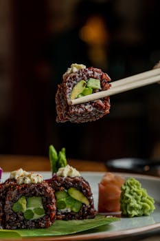 Close-up of a vegetarian sushi roll with avocado and asparagus, held by chopsticks.