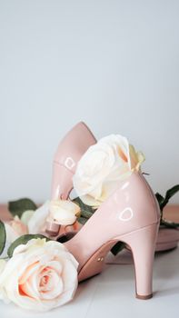 Elegant pink high heels adorned with soft pastel roses on a white background for fashion photography.