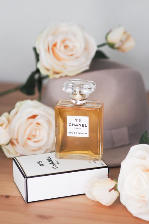 Free Chanel No. 5 perfume bottle surrounded by elegant roses on a wooden table. Stock Photo