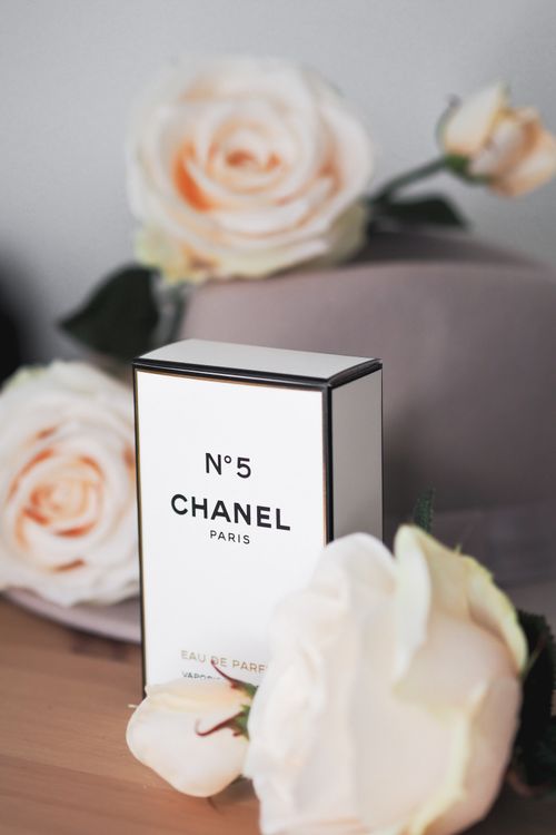 Free Chanel No. 5 perfume box surrounded by soft pink roses, creating a luxurious atmosphere. Stock Photo