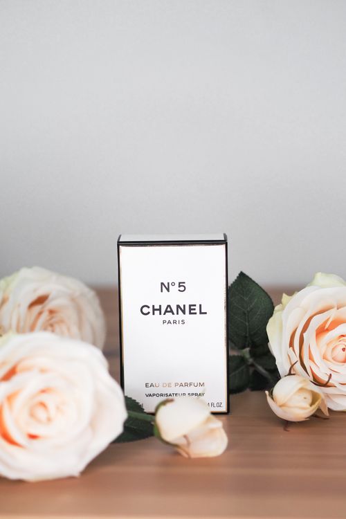 Free Chanel No. 5 perfume box surrounded by elegant white roses on a wooden surface, studio setting. Stock Photo
