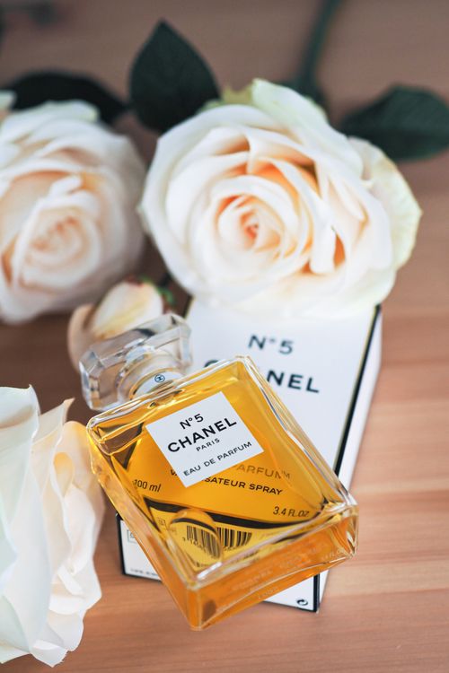 Free Chanel No. 5 perfume bottle surrounded by delicate white roses on a wooden surface, Parisian elegance. Stock Photo