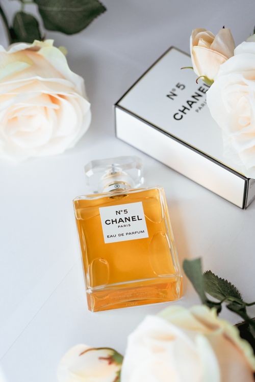 Free Elegant Chanel No. 5 perfume bottle surrounded by soft white roses, capturing luxury and fragrance. Stock Photo