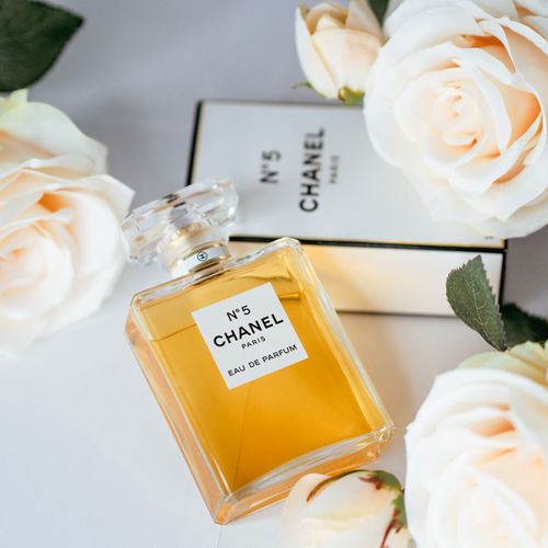 Free Chanel No. 5 perfume bottle on a white surface surrounded by roses, showcasing luxury and elegance. Stock Photo