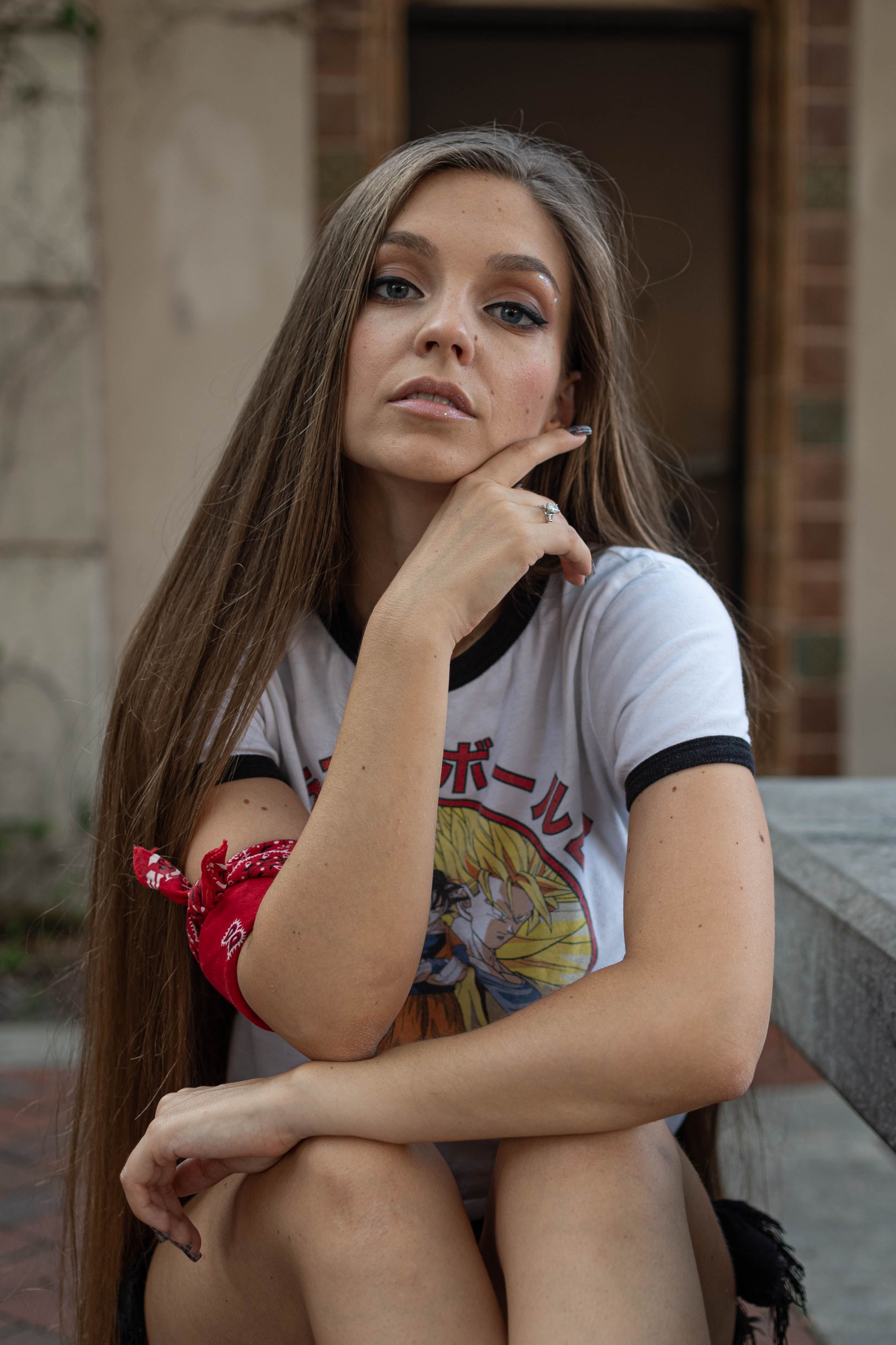 Stylish brunette woman sits outdoors, sporting an anime T-shirt and red bandana.