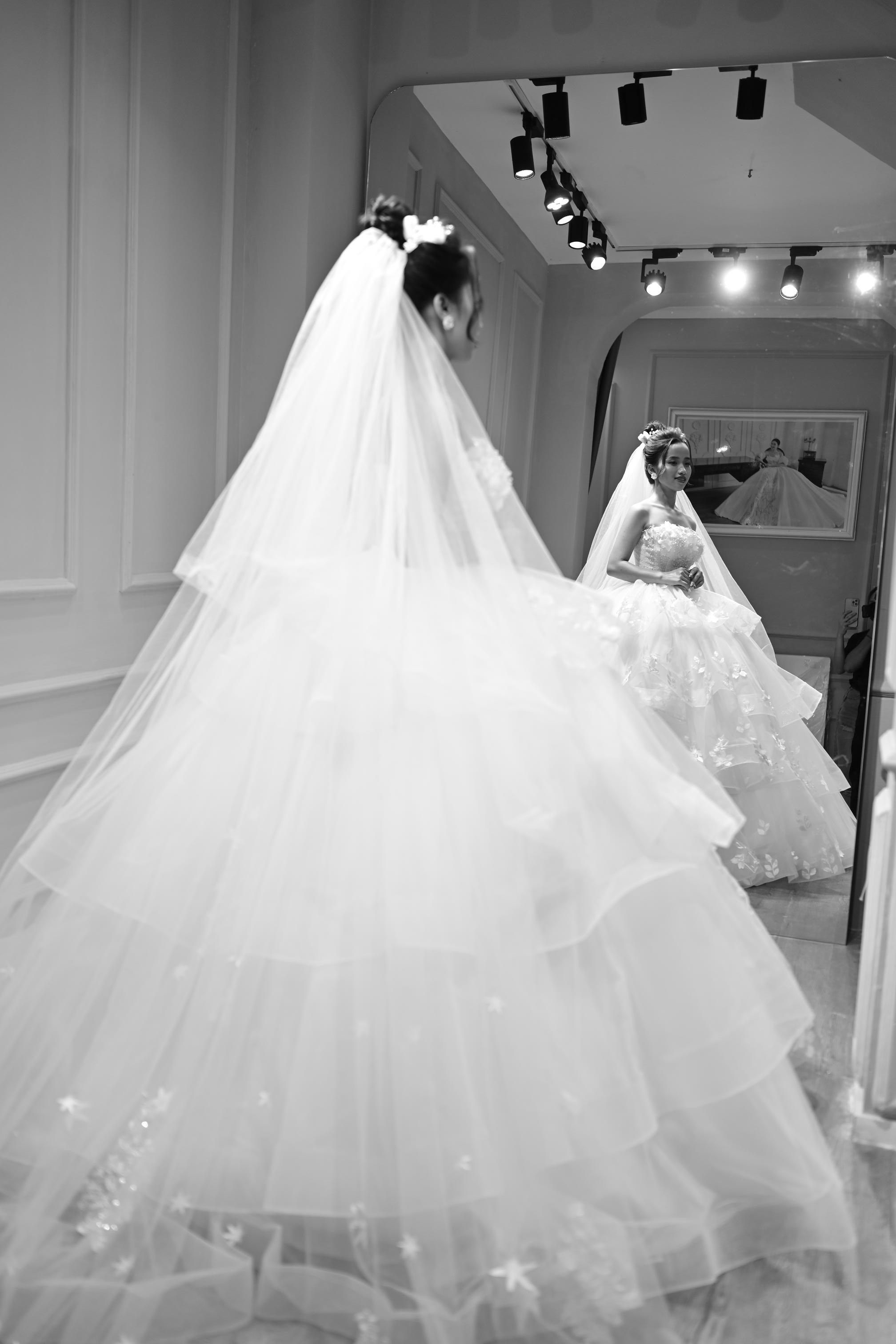 Elegant bride in a wedding dress admires her reflection in a mirror, captured in black and white.