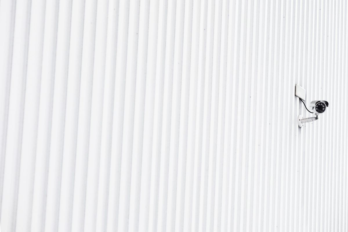 A compact wireless security camera mounted under the eaves of a home, facing the driveway