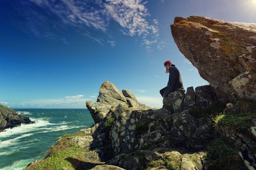 Man Sitting on Creek in Front of Body of Water