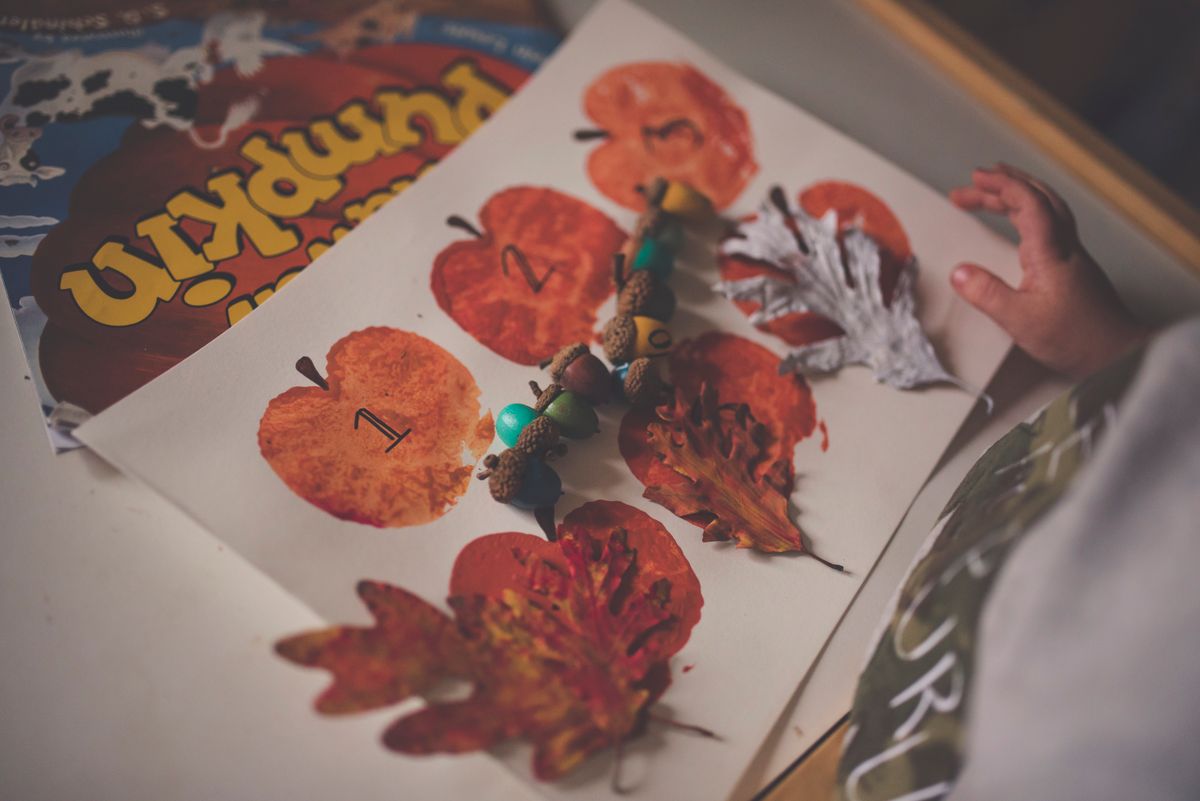 Fall-themed kids craft with apple stamp prints, pumpkins, and painted leaves