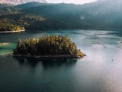 宁静湖泊被郁郁葱葱的群山环绕，湖中一座覆盖着茂密树木的岛屿，从空中俯瞰，景色静谧