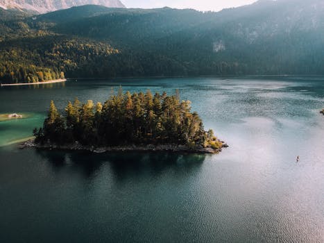宁静湖泊被郁郁葱葱的群山环绕，湖中一座覆盖着茂密树木的岛屿，从空中俯瞰，景色静谧
