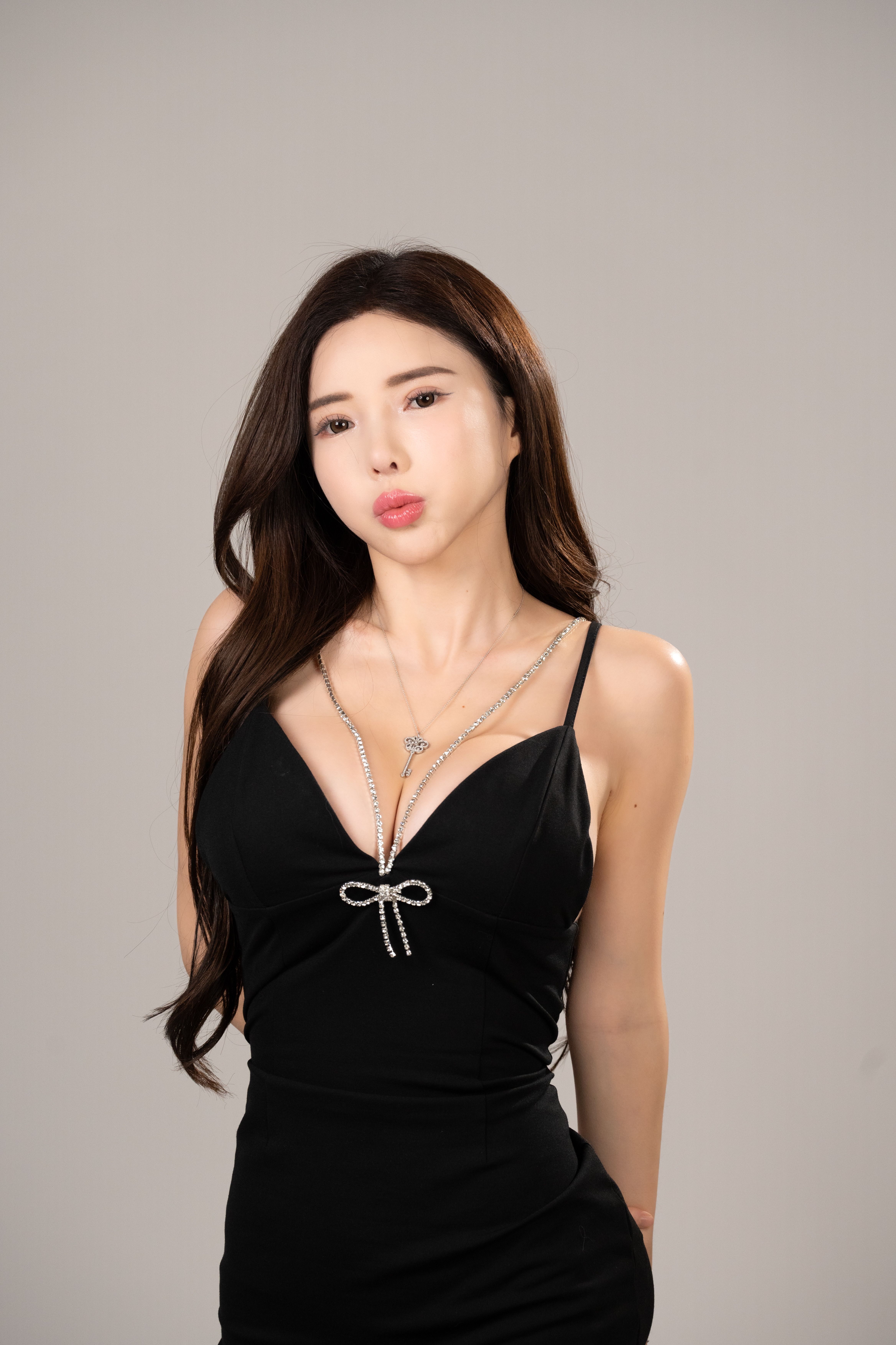 Stylish Asian woman in a black dress posing against a neutral studio backdrop, showcasing elegance and fashion.