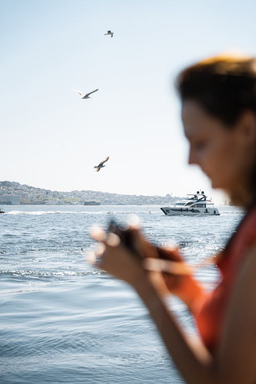 A woman taking a picture of a boat and birds