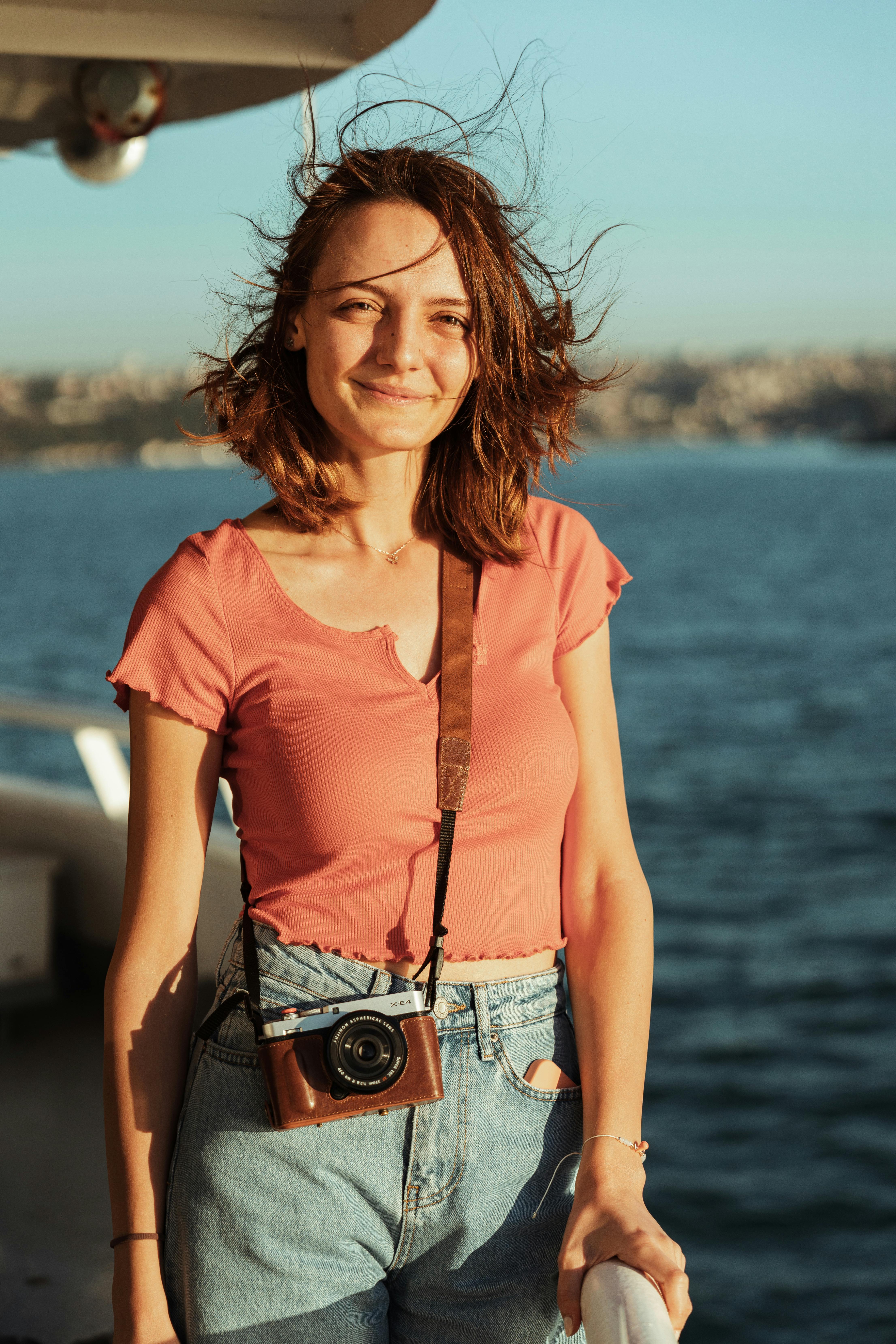 A young woman enjoying a summer boat ride, smiling with a camera around her neck.