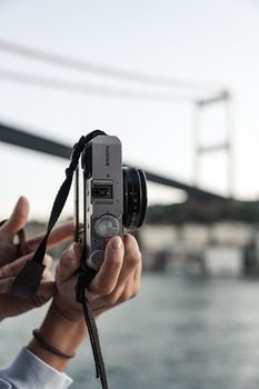 Close-up of hands holding a camera with a suspension bridge in the background.