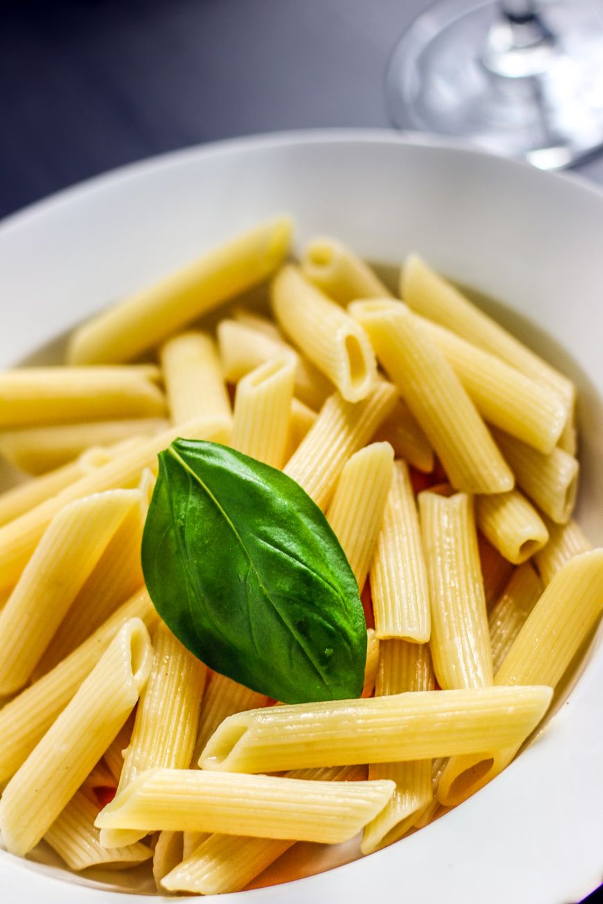 A bowl of golden penne pasta coated in vibrant red tomato sauce, garnished with fresh green basil leaves and a sprinkle of grated Parmigiano-Reggiano cheese