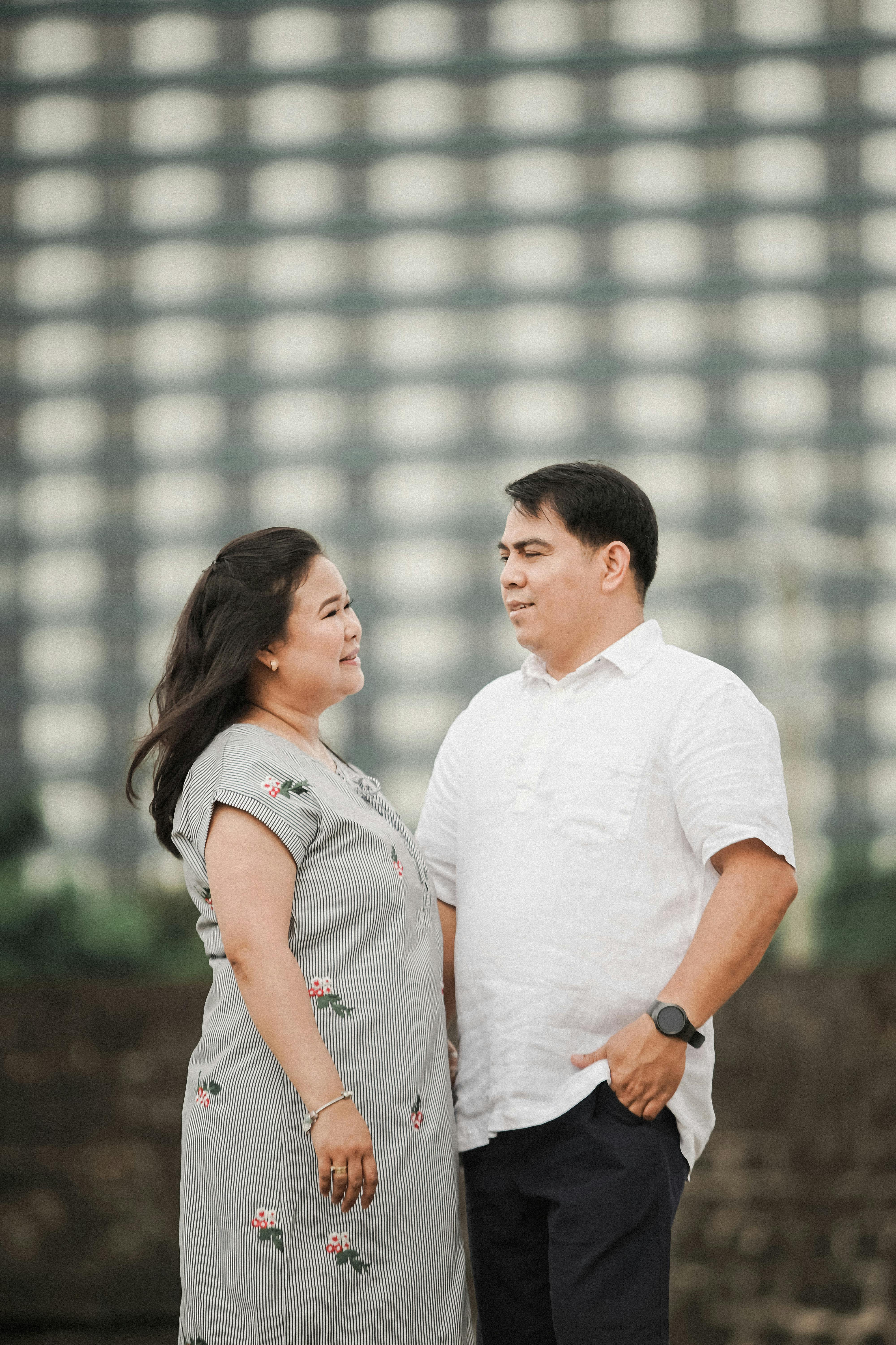 Smiling couple in casual attire standing outdoors against a cityscape background.