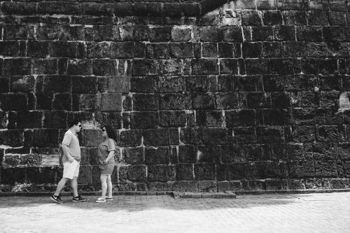 Free Two people standing in front of an ancient stone wall in an urban setting. Stock Photo