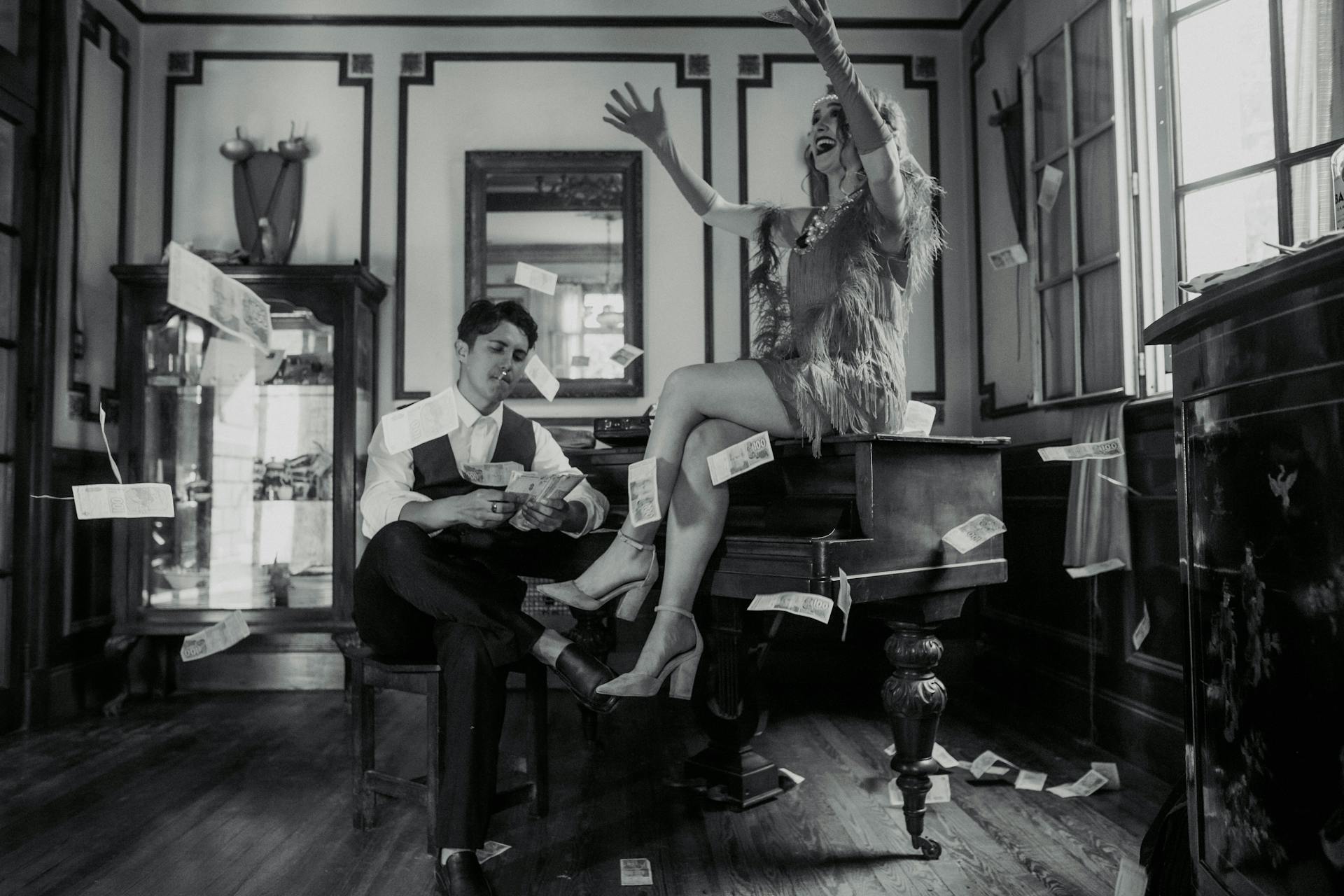 Black and white vintage scene with a glamorous couple throwing money indoors.