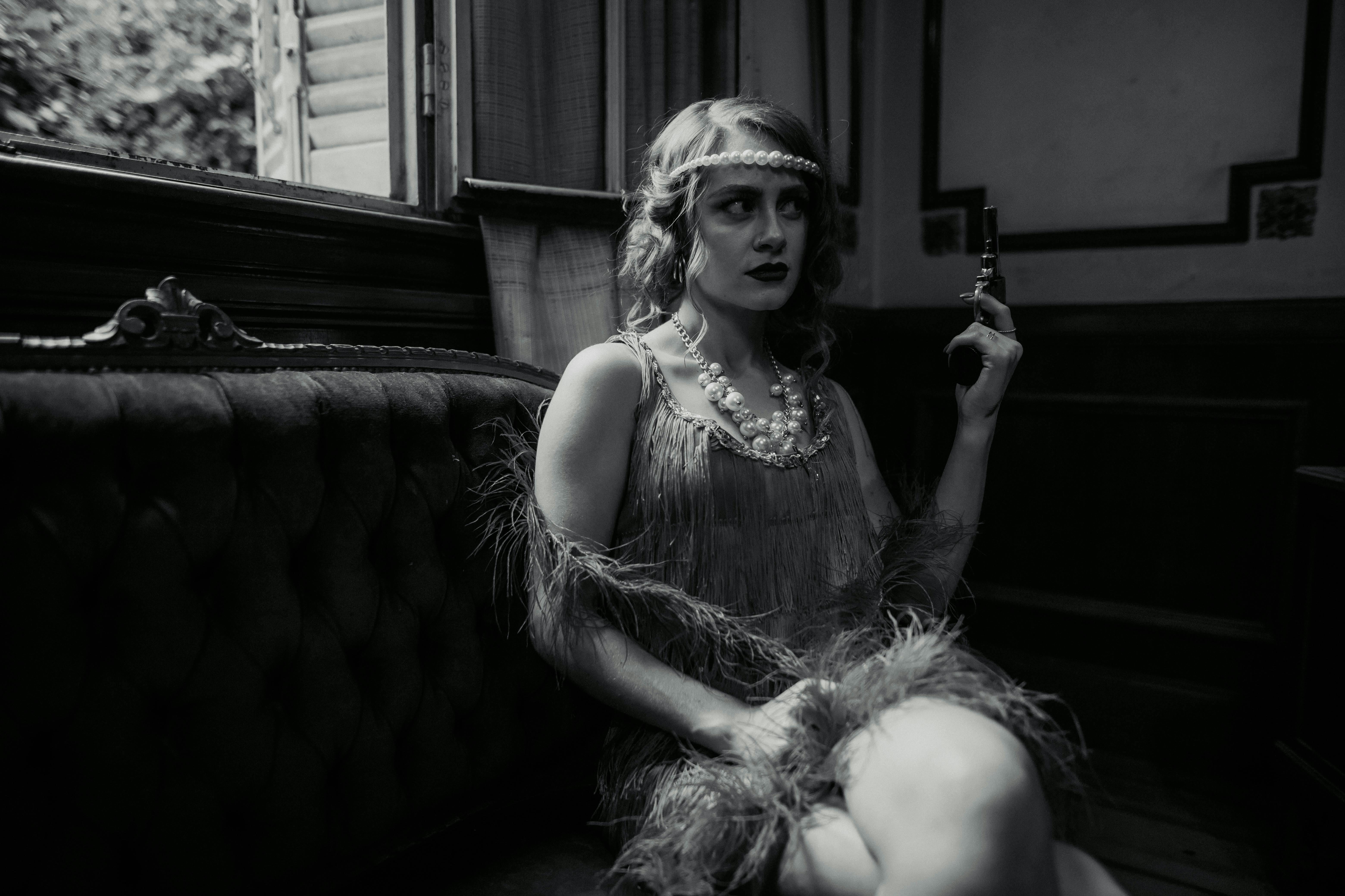 Artistic black and white portrait of a woman in vintage attire holding a gun.