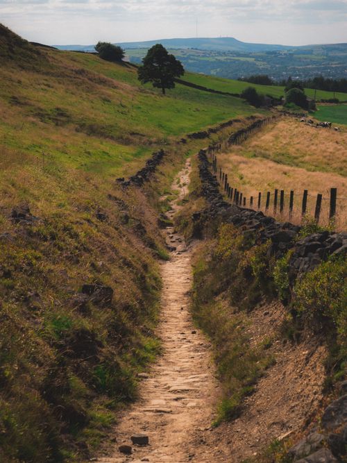 Free Idyllic rural path with stone fence, fields, and distant hills under a cloudy sky. Stock Photo