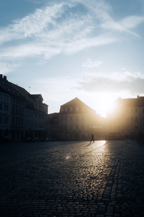 A person walking in the sun on a cobblestone street