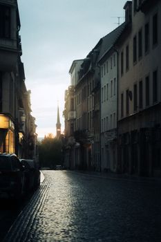 Cobblestone street in Zittau, Germany at sunset with historic architecture and a church tower.
