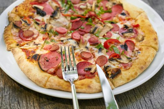 Close-up of a delicious pepperoni and mushroom pizza with sliced toppings on a rustic plate.
