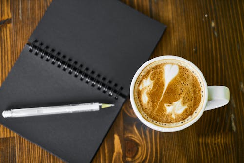 White Ceramic Mug Beside Black Covered Book