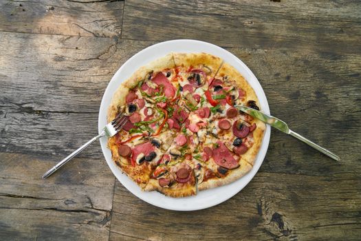 Top view of a pepperoni pizza with utensils on a rustic wooden table.