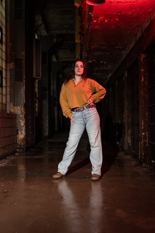 A woman in jeans and an orange shirt stands in an old warehouse