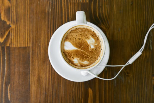 Top view of a cappuccino with latte art on a wooden table, accompanied by earphones.