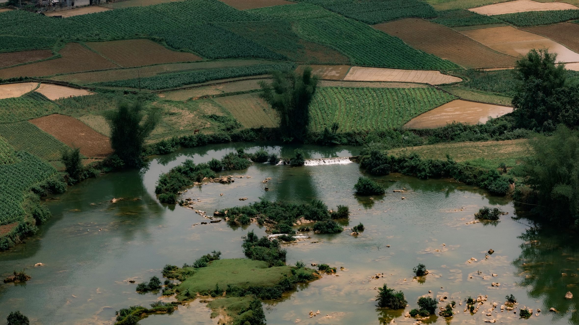 Aerial landscape of lush fields and river in Cao Bang, Vietnam, showcasing rural beauty.