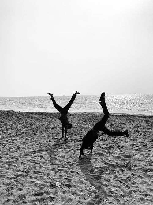 Free A monochrome capture of two people doing cartwheels on a sandy beach in Bali. Stock Photo