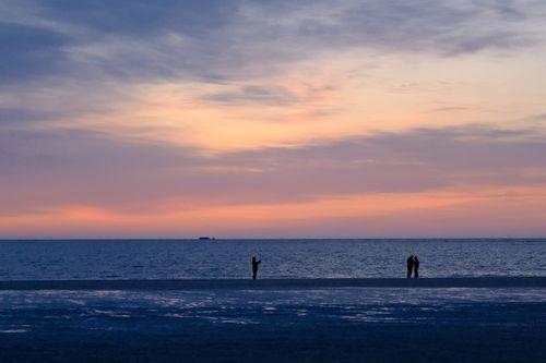 Free Silhouetted figures stand on a peaceful beach during a vibrant sunset over the ocean. Stock Photo