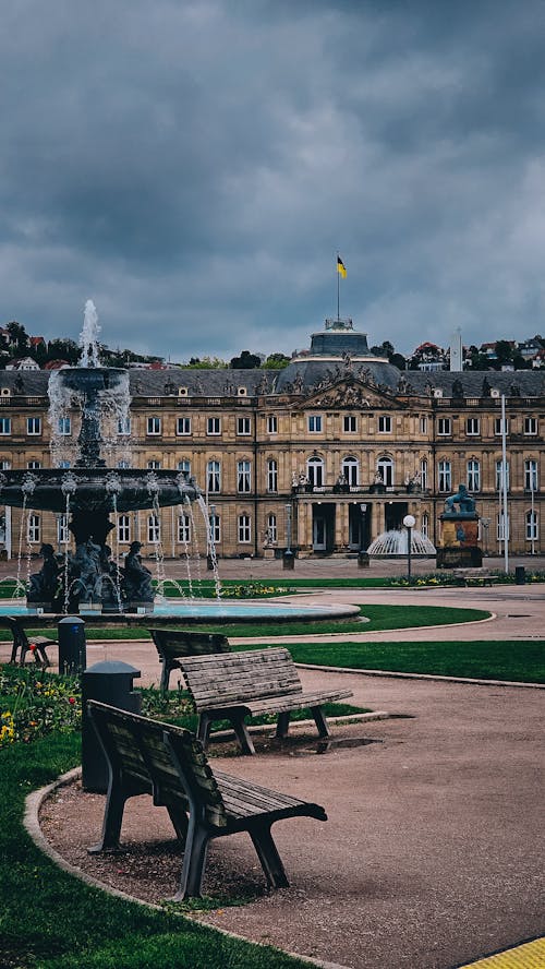 A park with benches and a fountain in front of a large building