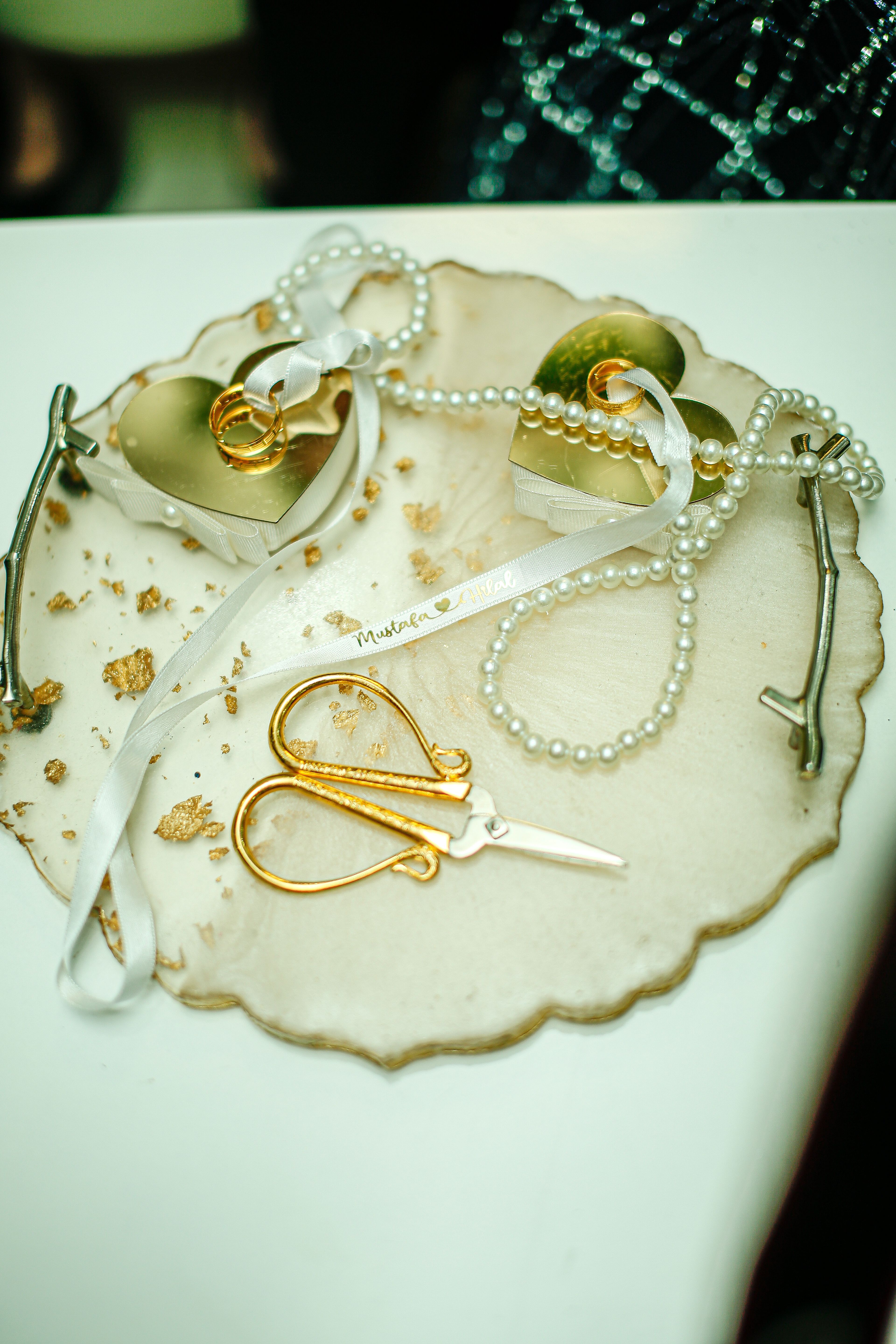 Top view of wedding accessories like ribbons, pearls, and scissors on a decorative plate.