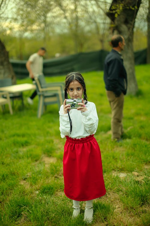 A young girl in a red skirt taking a picture